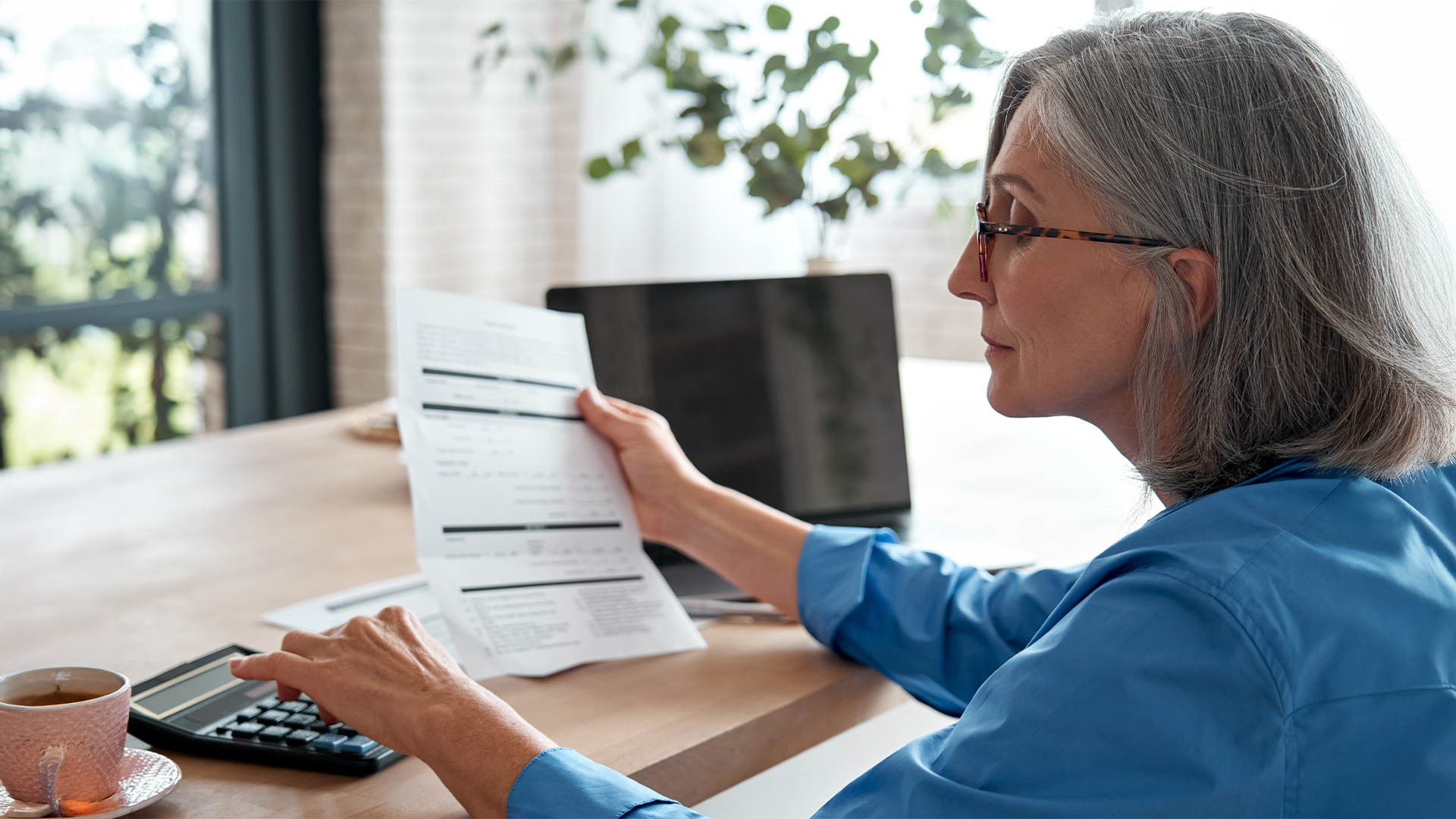 Senior mature business woman holding paper bill using calculator