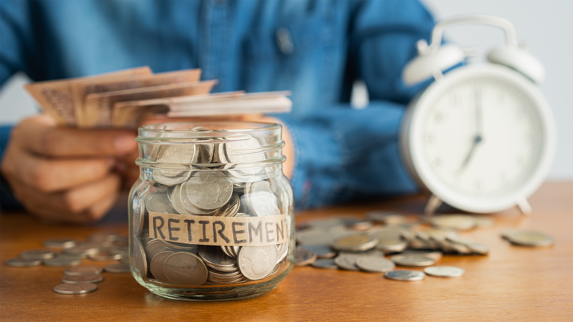 Coin in a glass bottle Image blurred background of business people sitting counting money and a retro white alarm clock, retirement, finance and saving money for future concept.